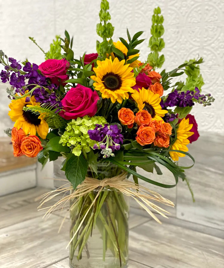 Vase of sunflowers, roses, hydrangeas and bells of Ireland on a shelf inside a florist in clayton, nc