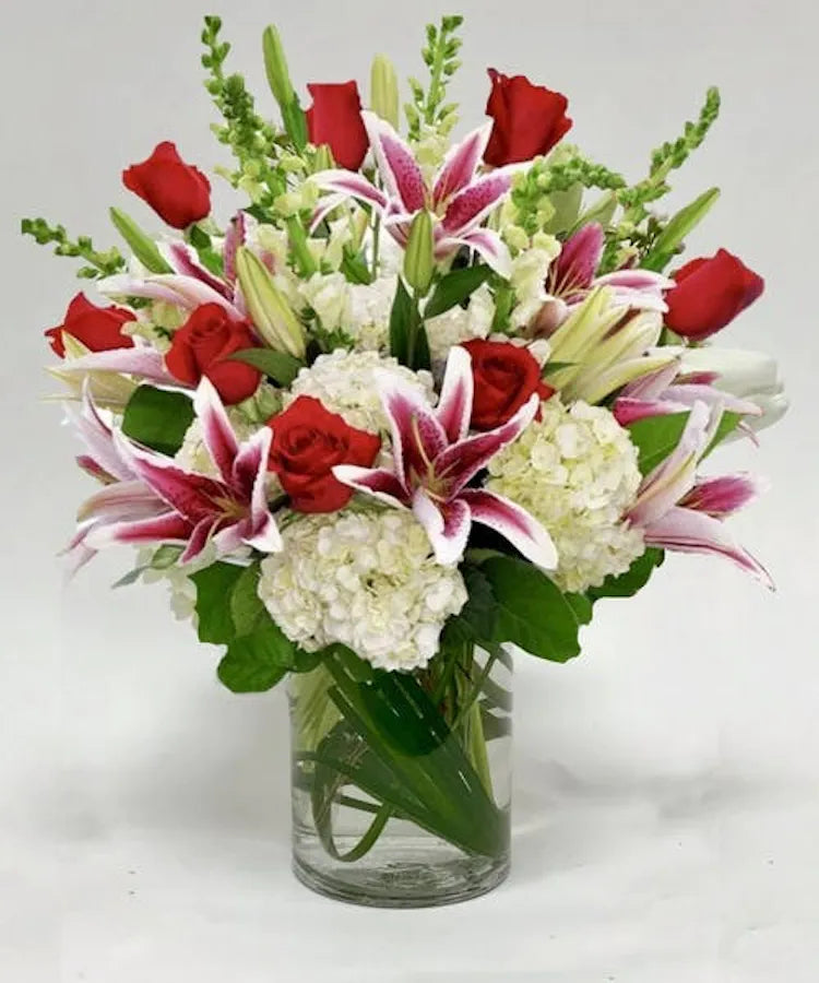Vase of stargazer lilies, hydrangeas, snapdragons & red roses on a table inside a florist in clayton, nc